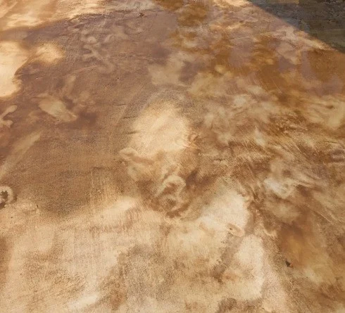 A floor covered in brown silt and sand, marked with drag streaks and dried tide lines, with shallow dirty water lying in the low points.
