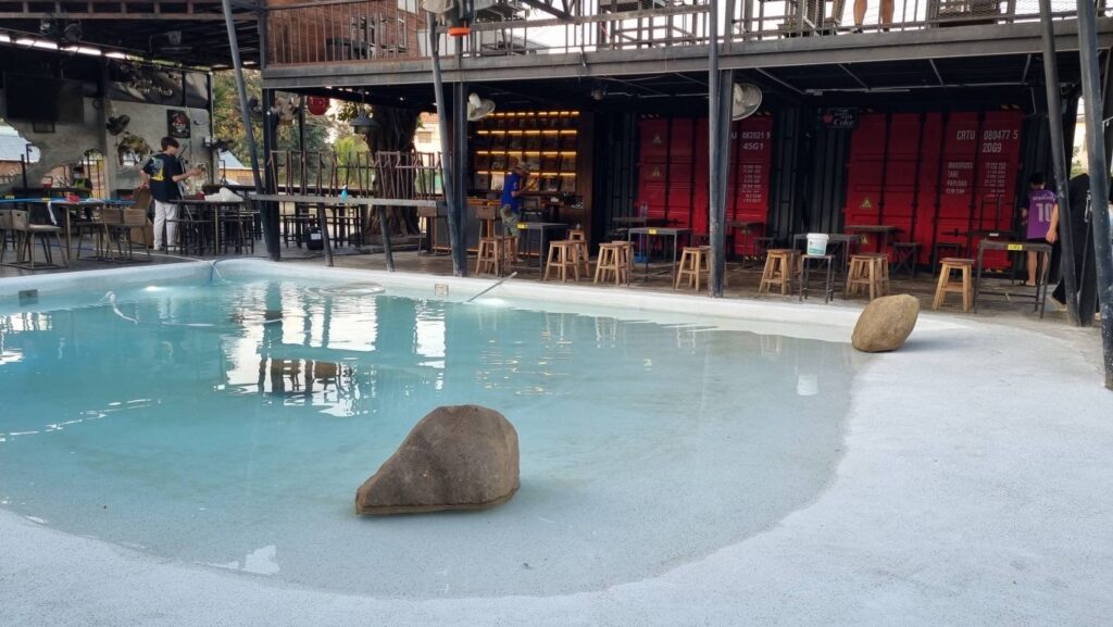 Daylight view of a curved shallow pool entrance with Cool Blue finish and decorative boulders at Beach Bar.