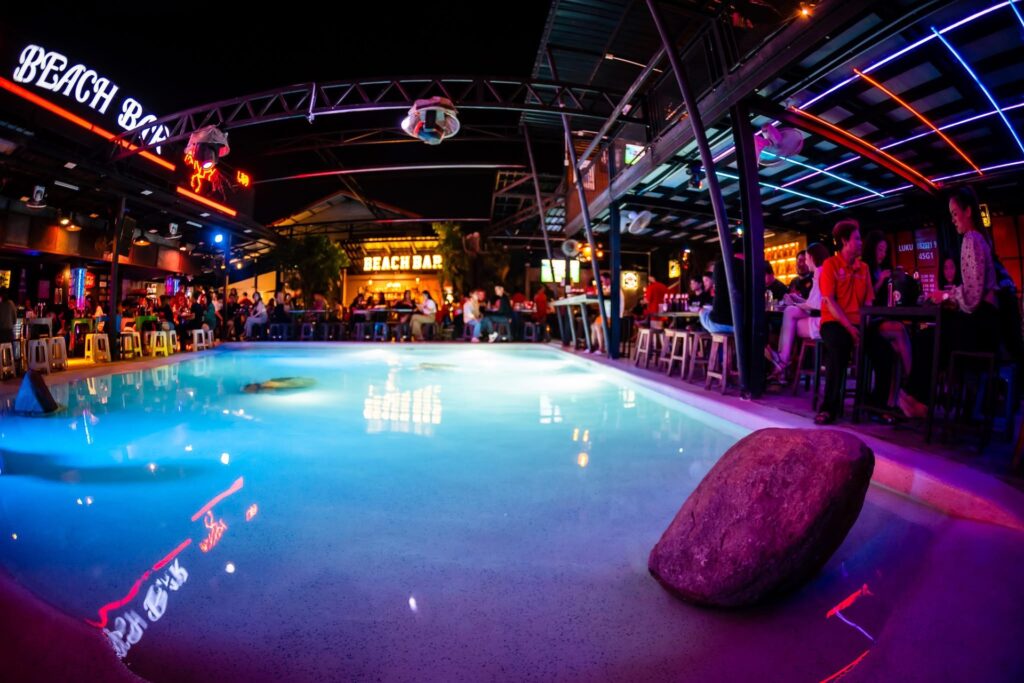 Freeform pool and shallow edge at Beach Bar illuminated by blue and magenta lighting at night.