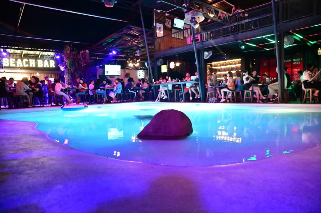 Low evening view across the illuminated shallow pool edge and a decorative boulder at Beach Bar.