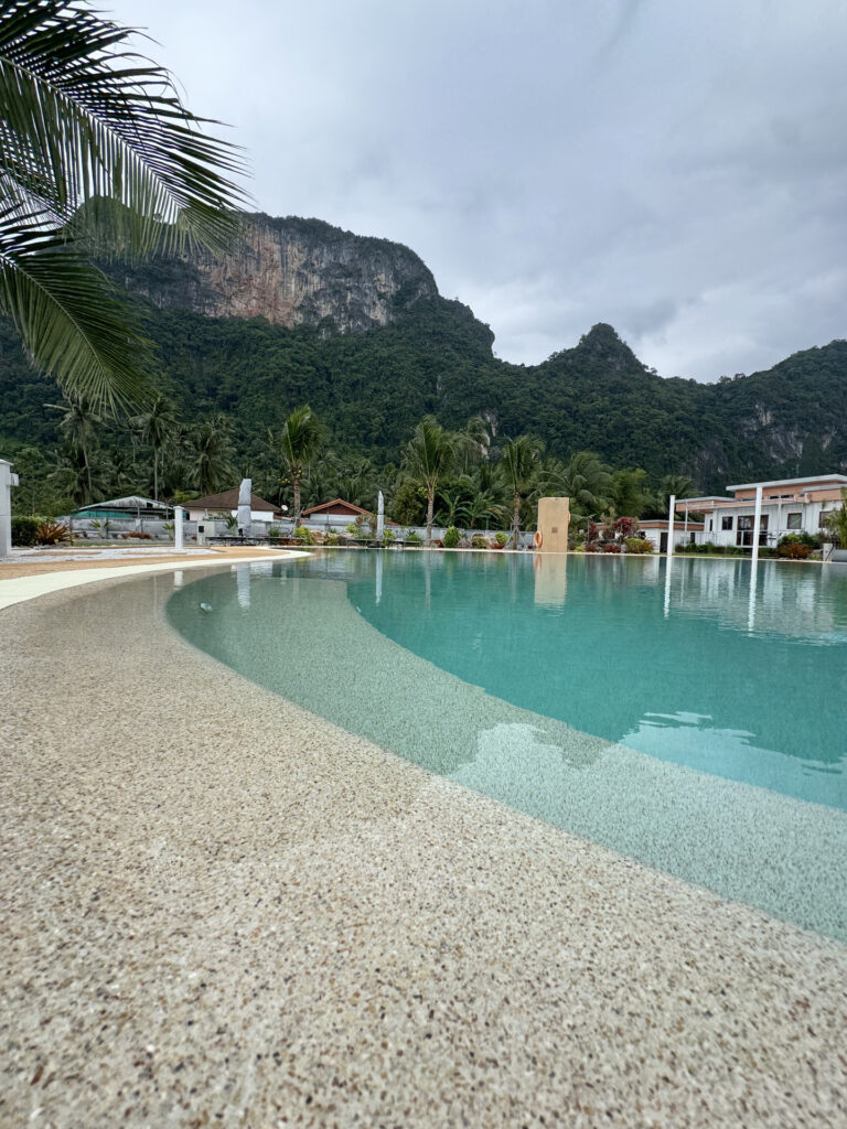 Low close view of the aggregate pool edge at This Great Place Resort, with the curved waterline and mountain setting beyond.