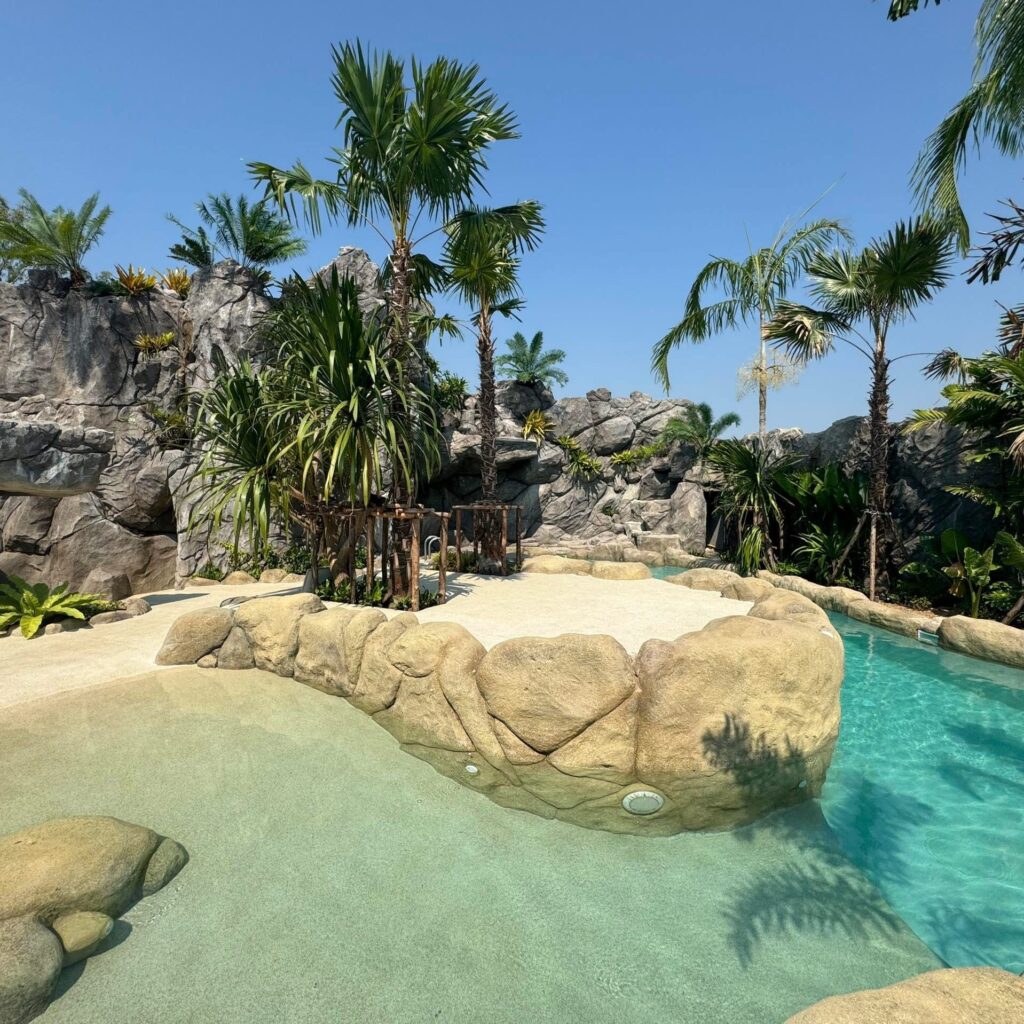 Wide view of a shallow lagoon-pool entrance curving around a palm-planted island.