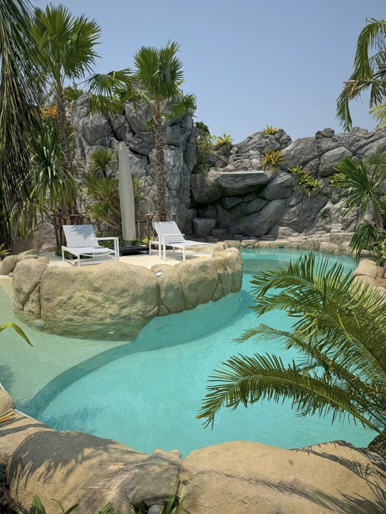 Curving turquoise pool around a rock-edged island with palms and two sun loungers.