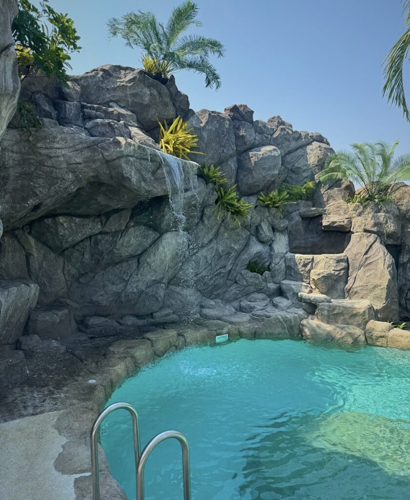 Waterfall spilling from a rock ledge into the lagoon pool beside a stainless-steel ladder.