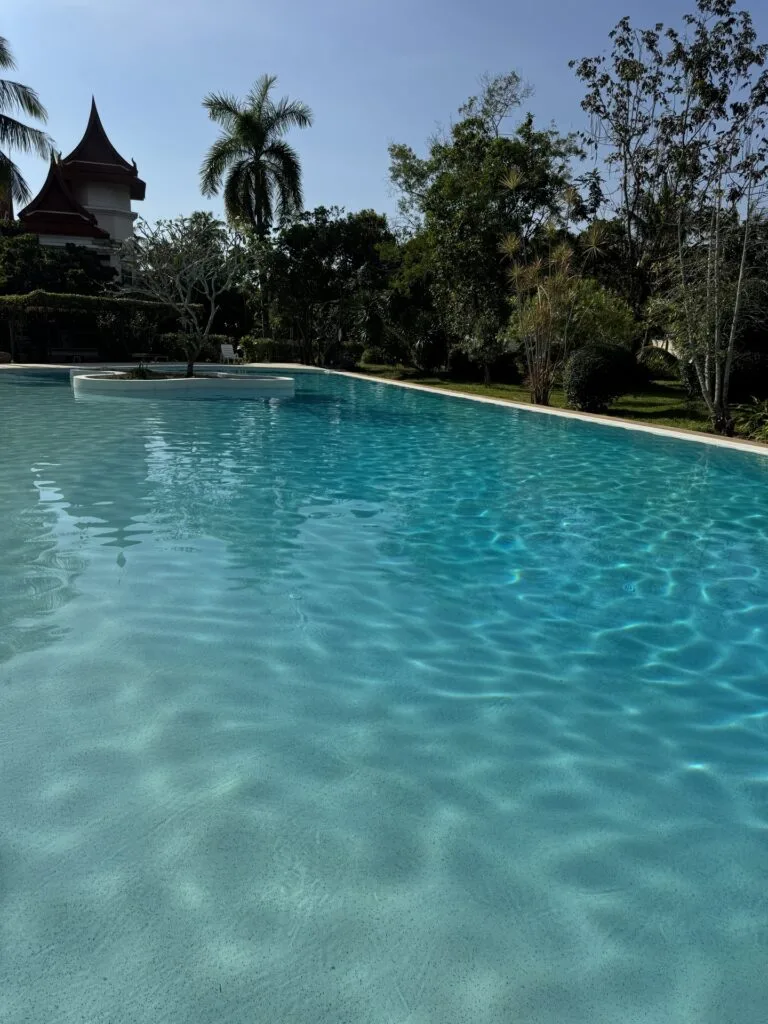 Sunlight ripples across the pale underwater finish, with tropical gardens around the shared pool.