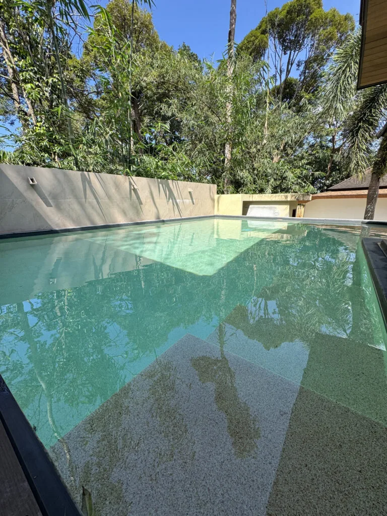 Submerged Polar White pool steps and tree reflections at a private villa in Phuket