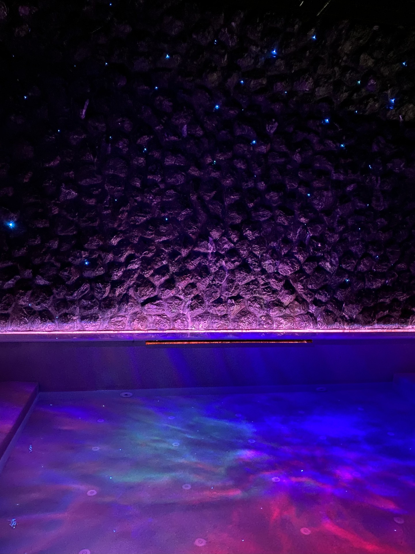 Coloured projection across a pale pool finish at a private villa in Phuket, with blue light points on the wall beyond