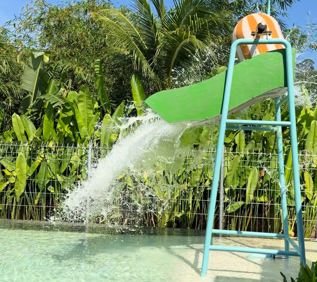 Tipping bucket sending water down a green chute into the splash-park pool at Sugar Marina Lagoon, Phuket.